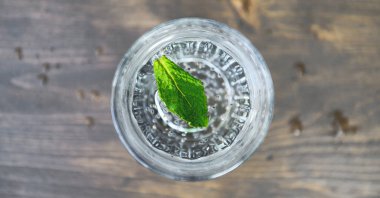 Ahşap zemin üzerinde nane yaprakları olan saf soğuk su. Detoks teması. Seçici odak.