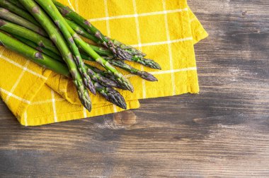 Tahta masadaki sarı peçetenin üzerinde bir sürü taze kuşkonmaz. Fotoğraf seçici bir odak ile çekildi.