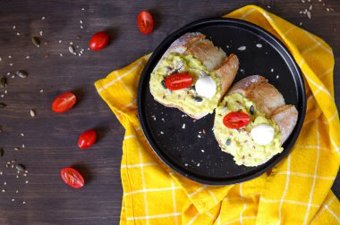 Avokado ve kiraz domatesli iki sandviç keten, susam, balkabağı tohumlu mozzarella ve sarı peçeteli ahşap bir masanın üzerinde siyah bir seramik tabakta yarım ayçiçeği. Düz yatıyordu.