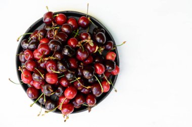 Beyaz ahşap arka planda seramik siyah bir tabakta sulu, olgun, güzel bir kiraz. Boşluğu kopyala.