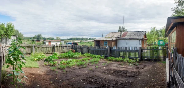 Panorama de terra agrícola na aldeia russa para paisagismo no jardim atrás da cerca com baldes e edifícios, celeiros, sob um céu nublado com campos e copses no horizonte . — Fotografia de Stock