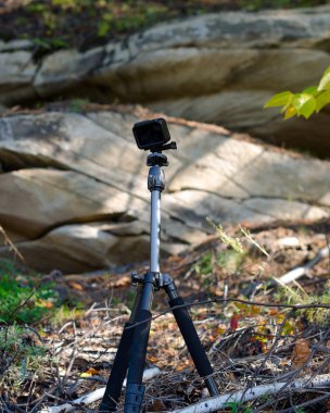 Aksiyon kamerası şişkin kayanın oradaki ormanda bir tripod kayıt videosunun üzerinde duruyor..