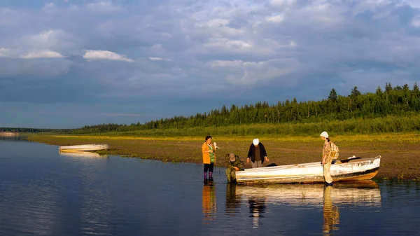 stock image Three Yakut women and one Yakut man tinkering at a boat on the banks of the Northern Viluy river at sunset.