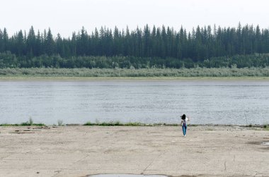 The girl-traveler goes to the edge of the concrete sidewalk, touching the hair on the shore of the pier North of the vilyu river with spruce forests and the tundra of Yakutia on the other side of the shore.