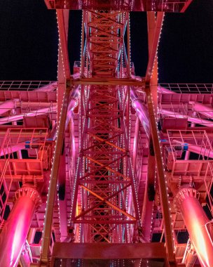 Büyük metal bir yapıya sahip parlak kırmızı bir dönme dolap parıldıyor ve karanlıkta aydınlık bir kutlama yaratıyor..