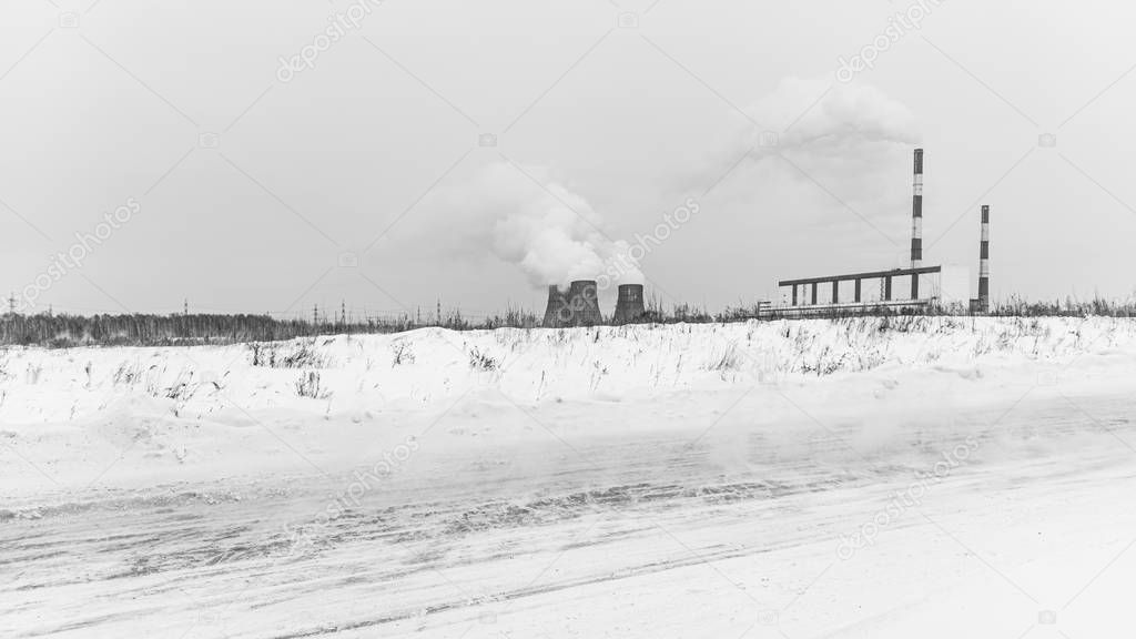 The road with snow drifts goes against the background of Large boilers of a powerful thermal power station on coal smoke in the sky in the winter in the city of Novosibirsk on the field.
