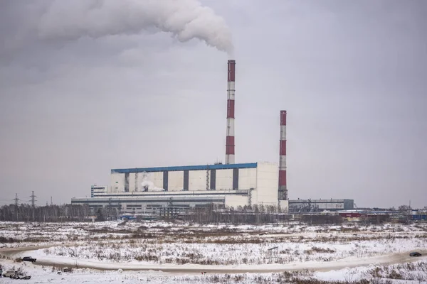 The road with snow drifts and fast cars goes against the background of Large boilers of a powerful thermal power station on coal smoke in the sky in the winter in the city of Novosibirsk on the field.