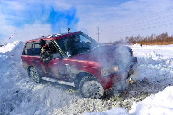 俄罗斯 Novosibirsk March 2020 一辆四轮驱动的越野车正驾驶着一辆四轮驱动的越野车在雪山上行驶 车顶着蓝色的浓烟 一个头戴硬礼帽的男子正在外面看着路 — 图库照片