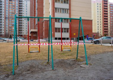 Novosibirsk, Rusya-12 Nisan 2020. Çocuklar sokakta salıncakların önünden koşuyorlar. Oyun bahçesinde, çizgili bantlarla kaplı bir apartmanın bahçesinde. Topluma kapalı..