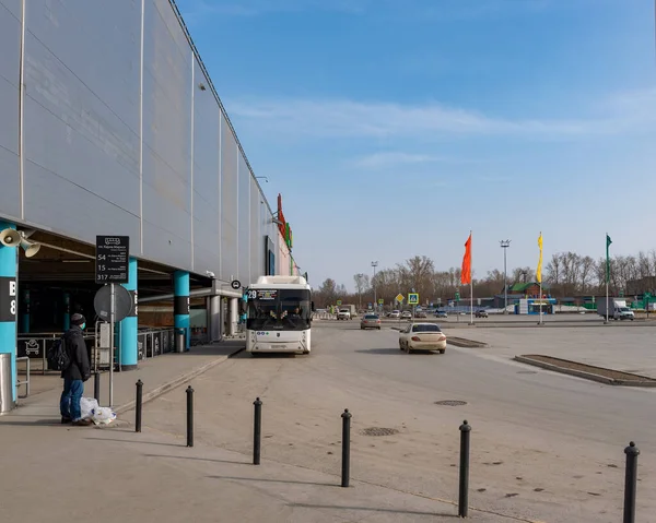 Novosibirsk, Rusya-12 Nisan 2020. Tıbbi maskeli yalnız bir adam Auchan Hipermarket 'te market poşetleriyle duruyor. Kovid 19 virüs salgınının karantinasından dolayı otobüs beklemeyi bırakın..