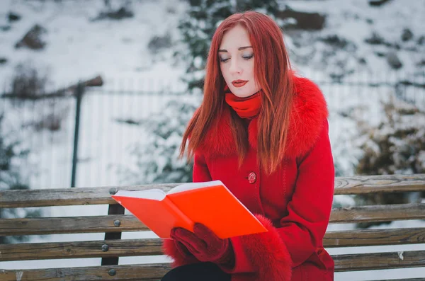 Jeune femme aux cheveux roux en manteau rouge dans la forêt d'hiver avec un bo — Photo