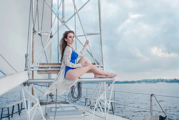 Relaxed girl sitting on sailboat, enjoying mild sunlight, fashion model in luxury sea cruise, summer vacation and travel.