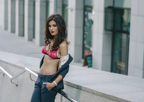 Una atractiva morena delgada en un sujetador rojo y pantalones se encuentra en la calle de la ciudad. Foto de moda —  Fotos de Stock