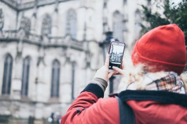 Slovakya 'nın Kosice kentinde, cep telefonuyla Gotik katedralin fotoğrafını çeken kırmızı ceketli bir kadın.