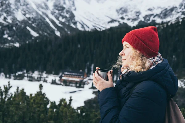 Mujer tomando una bebida caliente de la taza termo con vistas a los picos nevados de las montañas de Tatra — Foto de Stock