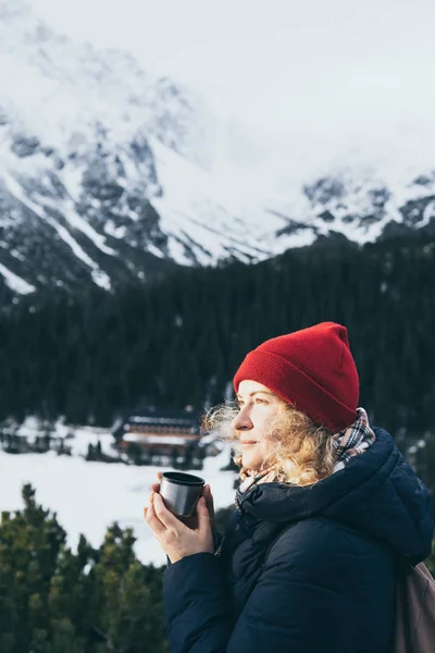 Mujer tomando una bebida caliente de la taza termo con vistas a los picos nevados de las montañas de Tatra — Foto de Stock