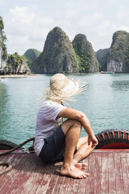 Hasır şapkalı genç adam Lan Ha Bay, Cat Ba Adası, Vietnam 'da tekne gezisinin tadını çıkarıyor.