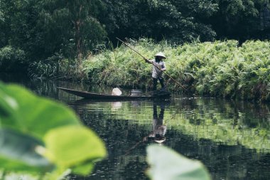 Ninh Binh, Vietnam - Mayıs 2019: Vietnamlı kadın Trang An doğa parkında tahta bir sandalda balık tutuyor.