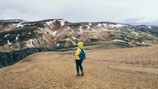 Sarı yağmurluklu kadın Landmannalaugar Ulusal Parkı, İzlanda 'da renkli dağlarda yürüyüş yapıyor. — Stok fotoğraf