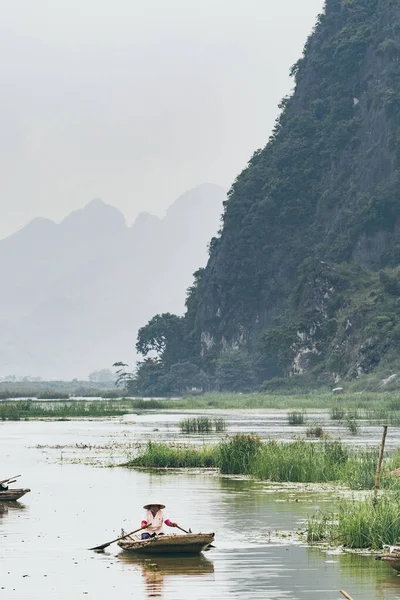 Ninh Binh, Vietnam-maj 2019: vietnamesisk kvinna i en trä roddbåt som går genom Trang An Nature Park — Stockfoto