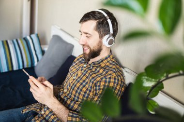 Evdeki koltukta kulaklıkla müzik dinleyen bir adam cep telefonu ekranına bakıyor.