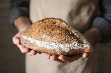 Kırsal önlüklü bir adam elinde bir somun ekmek tutuyor. Ürünü kapat..
