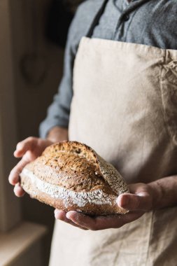 Kırsal önlüklü bir adam elinde bir somun ekmek tutuyor. Ürünü kapat..