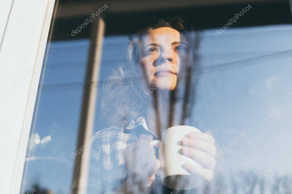 Young blonde woman looking out of the window with a concerned expression on her face. Reflection in the glass, double exposure effect