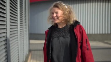 Genç sarışın kadın şehir ortamında kablosuz kulaklıkla müzik dinlerken dans edip zıplıyor. Yavaş çekim