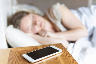 Ön planda cep telefonuyla uyuyan Doğu Avrupalı genç bir kadın..
