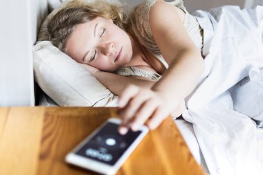 Doğu Avrupalı genç bir kadın yatakta uzanıyor ve sabahları cep telefonunun alarmını kapatıyor..