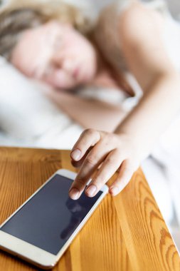 Doğu Avrupalı genç bir kadın yatakta uzanıyor ve sabahları cep telefonunun alarmını kapatıyor..