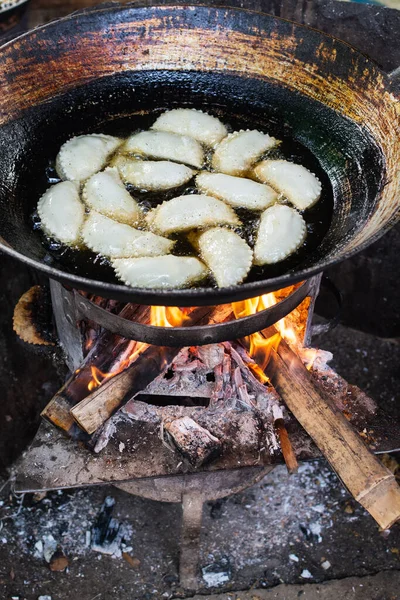 Dough dumplings frying in oil on wood burning stove. Asian food stalls in the market of Indein, Myanmar. Vertical orientation