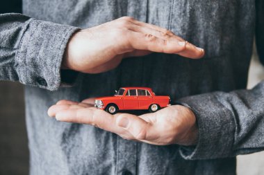 Erkek el ele tutuşup kırmızı bir oyuncak arabayı koruyor. Sigorta ve yol güvenliğinin kavramsal görüntüsü.