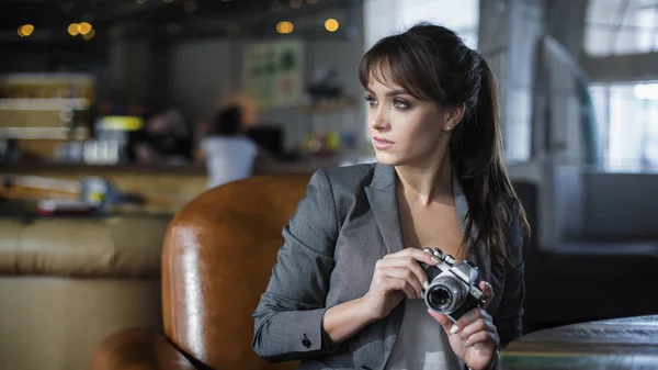 Портрет молодого фотографа-подростка с длинными волосами с фотокамерой в кафе. Красивая девушка держит в руках старую аналоговую кинокамеру и смотрит на видоискатель  . — стоковое фото