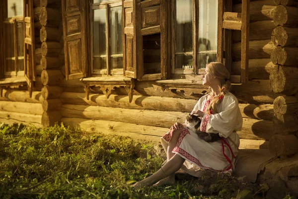 Mujer rusa con un gato cerca de la vieja casa de madera en un pueblo —  Fotos de Stock