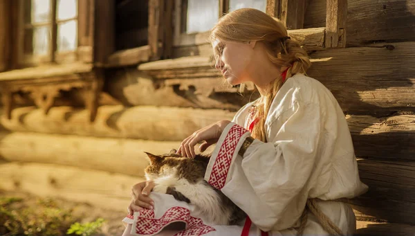 Mujer rusa con un gato cerca de la vieja casa de madera en un pueblo — Foto de Stock