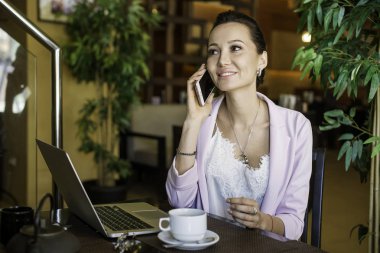 Kafede dinlenme sırasında hücre telefon ve dizüstü bilgisayar kullanan rüya gibi kadın büyüleyici kahvehane iç, taşınabilir net-kitap ile oturan genç güzel kadın