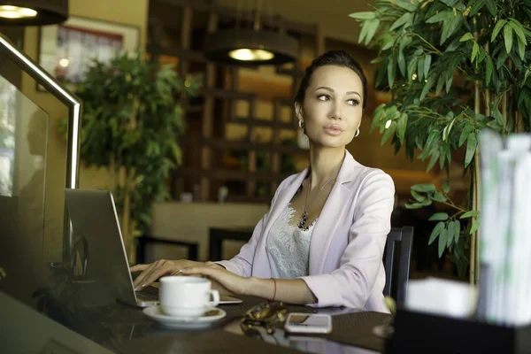 Jeune belle femme assise avec portable net-book dans l'intérieur du café, charmante femme rêveuse à l'aide de téléphone cellulaire et ordinateur portable pendant le repos dans le café — Photo