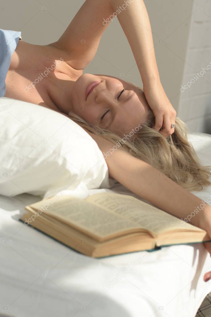beautiful blonde woman lying on the bed comfortably dreamig and read the book. smiling