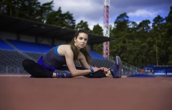 Mujer atlética estirando sus músculos antes de trotar en la pista — Foto de Stock