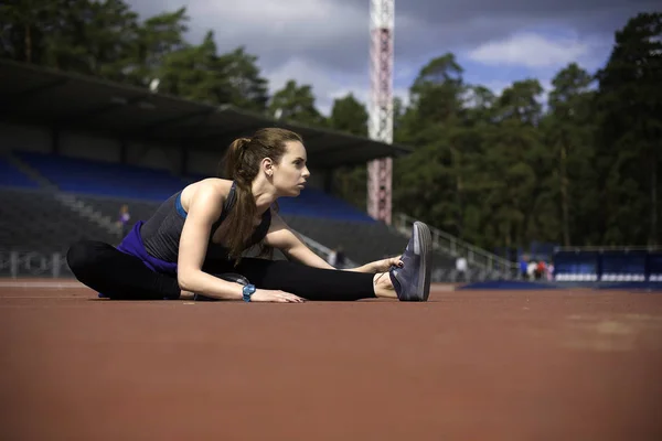 Mujer atlética estirando sus músculos antes de trotar en la pista — Foto de Stock