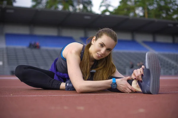 Mujer atlética estirando sus músculos antes de trotar en la pista — Foto de Stock