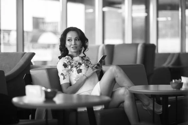 Young woman drinking coffee and use her smartphone sitting indoor in urban cafe. Cafe city lifestyle. Casual portrait of beautiful girl. Black and white — Stock Photo, Image