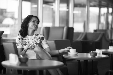 Genç kadın kapalı kentsel kafede oturan onun smartphone içme kahve ve kullanım. Cafe city yaşam tarzı. Güzel kız rahat portresi. Siyah ve beyaz