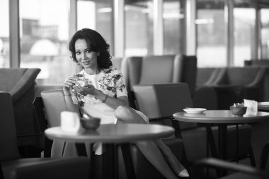 Genç kadın kapalı kentsel kafede oturan onun smartphone içme kahve ve kullanım. Cafe city yaşam tarzı. Güzel kız rahat portresi. Siyah ve beyaz