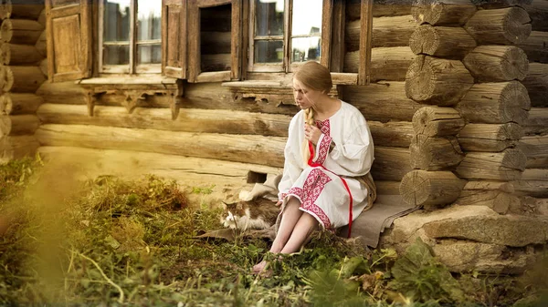 Mujer rusa con un gato cerca de la vieja casa de madera en un pueblo — Foto de Stock