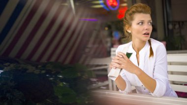 Genç rüya gibi güzel kadın yaz kafede oturur, sokağa bakmaktadır ve sıcak kahve latte bardaktan içer.