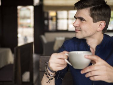 Genç çay ile restoranda oturan adam yorgun. Bak boynunda elini tutarak yorgun. Yorgunluk. Üzgün o gülüyor.