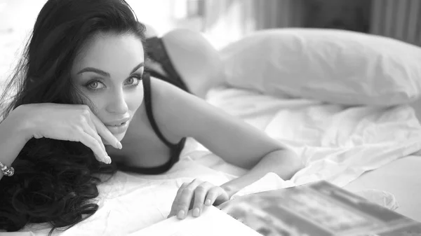 非常にセクシーなブルネットの女性は、黒の下着を着てベッドに横になっています。官能的なウェイク アップ、モノクロ画像 — ストック写真